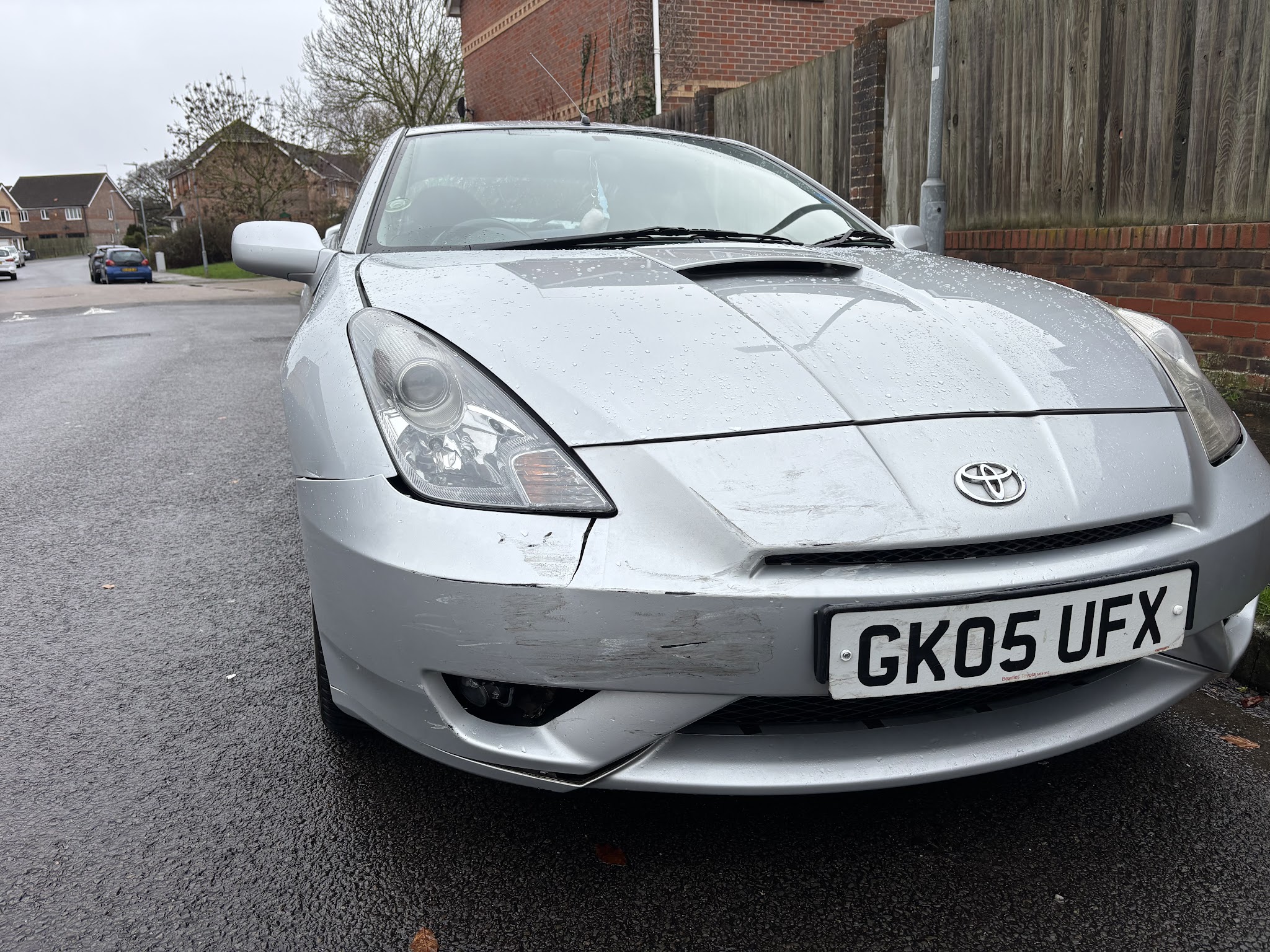 Silver Toyota Celica with a cracked, scraped front bumper and damaged wing before repair