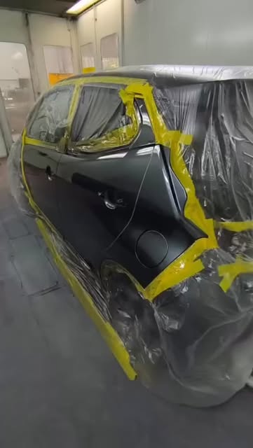 A car masked up in plastic and tape inside the spray booth, ready for paint