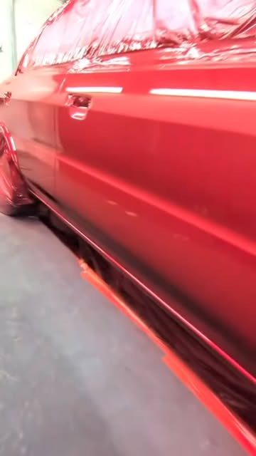 Freshly painted red car side under the spray booth lights